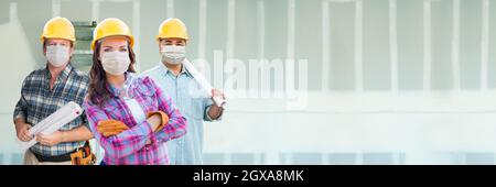 Weibliche und männliche Auftragnehmer in harten Hüten tragen medizinische Gesichtsmasken auf der Baustelle während Coronavirus Pandemie Banner. Stockfoto