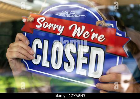 Weibliche Ladenbesitzerin, die das Schild zu „Geschlossen im Fenster“ umdreht. Stockfoto