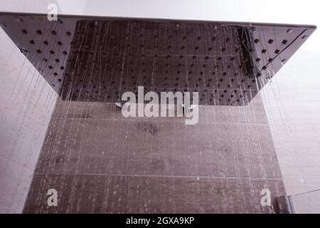 Moderne, elegante Edelstahldusche mit Wassertropfen im Bad Innenwasser, das vom quadratischen Duschkopf in einem modernen Bad strömt Stockfoto