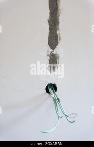 Buchsenleiste mit Kabeln in einer Wand. Kabelhintergrund: Elektrische Drähte, die aus der Öffnung der Steckdosen an der Wand herausragenbleiben. Neue elektrische Version Stockfoto