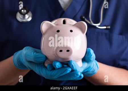 Doktor oder Krankenschwester tragen chirurgische Handschuhe Holding Piggy Bank. Stockfoto