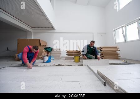 Fachkräfte, die die keramischen Holz-Effekt-Fliesen auf dem Boden Installieren, Arbeiter, die Laminatboden auf der Baustelle der neuen Wohnung machen Stockfoto