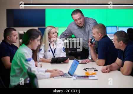 Eine Gruppe von Sicherheitskräften, die im Kontrollraum des Systems sitzen und eine Einweisung erhalten, arbeiten im Sicherheitsrechenzentrum, das von mehreren Bildschirmen umgeben ist Stockfoto