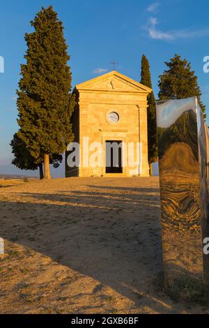 Alte Kirche von Vitaleta mit Bäumen auf beiden Seiten & Abbracio di luce von Helidon Xhixha in San Quirico d'Orcia, in der Nähe von Pienza, Toskana, Italien im September Stockfoto