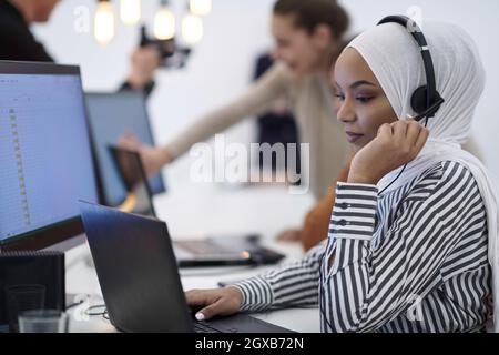 Schöne moderne afrikanische muslimische Geschäftsfrau im Büro, trägt Hijab und spricht auf einem Headset im modernen Startup Coworking Space Stockfoto
