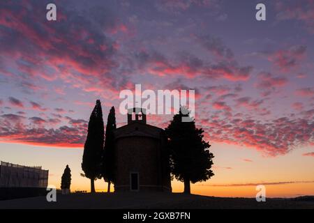 Atemberaubender Sonnenuntergang hinter der alten Kirche von Vitaleta mit Bäumen auf beiden Seiten in San Quirico d'Orcia, in der Nähe von Pienza, Toskana, Italien im September Stockfoto