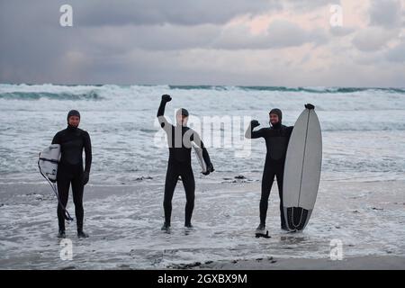 Authentische lokale arktische Surfer, die nach dem Surfen im Nordmeer am verschneiten Strand vorbei fahren. Norwegische Küste. Winter Wasseraktivitäten Extremsport Stockfoto