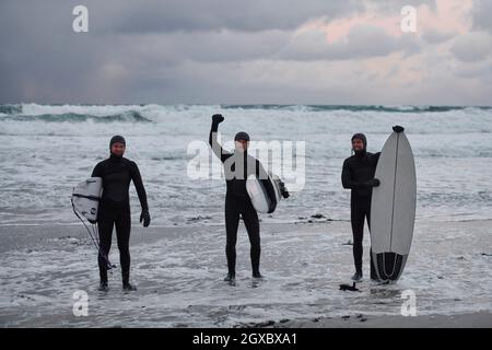 Authentische lokale arktische Surfer, die nach dem Surfen im Nordmeer am verschneiten Strand vorbei fahren. Norwegische Küste. Winter Wasseraktivitäten Extremsport Stockfoto