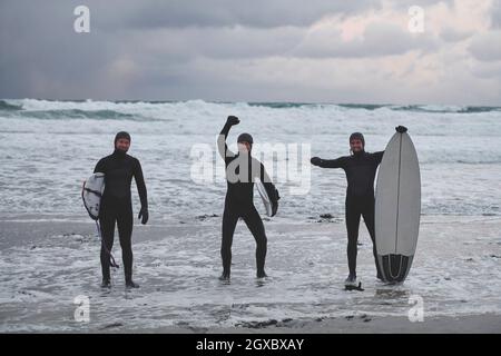 Authentische lokale arktische Surfer, die nach dem Surfen im Nordmeer am verschneiten Strand vorbei fahren. Norwegische Küste. Winter Wasseraktivitäten Extremsport Stockfoto