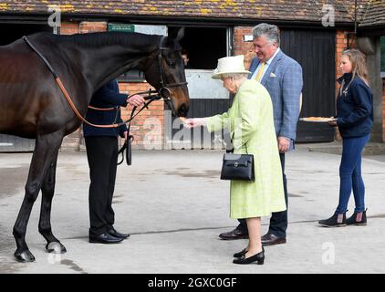 Königin Elizabeth II füttert ein Pferd mit einer Karotte, beobachtet von Trainer Paul Nicholls, während eines Besuchs im Manor Farm Stables in Ditcheat, Somerset, am 28. März 2019. Stockfoto