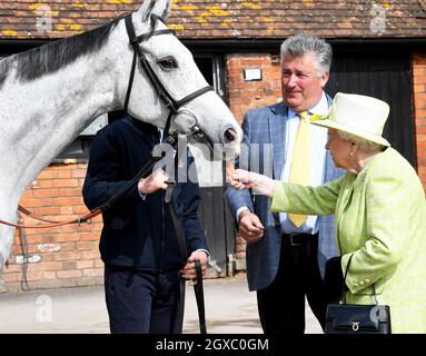 Königin Elizabeth II füttert ein Pferd mit einer Karotte, beobachtet von Trainer Paul Nicholls, während eines Besuchs im Manor Farm Stables in Ditcheat, Somerset, am 28. März 2019. Stockfoto