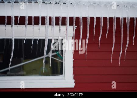 Eiszapfen auf dem Dach eines roten Hauses in Norwegen. Schmelzende Eiszapfen. Natürliche Eisbildung im Winter. Stockfoto