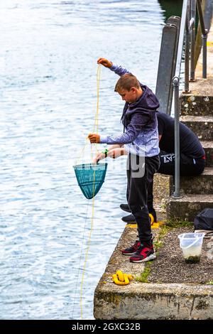 Zwei kleine Jungen, die in einem Hafen von Cornwall Krabben angeln. Stockfoto