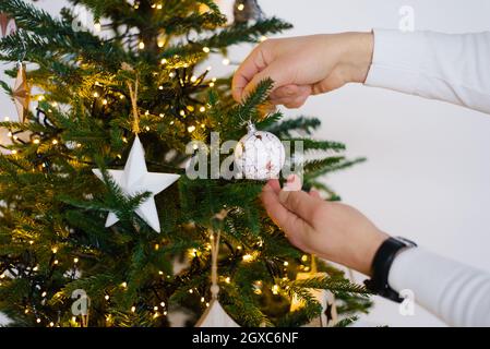 Ein Mann schmückt einen Weihnachtsbaum, hängt einen Ball an einen Weihnachtsbaum. Nahaufnahme der Hände Stockfoto