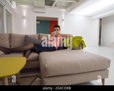 Junge Frau, die sich bei einem kostenlosen Teetrinken auf dem Ecksofa in einem großen, stilvollen Maisonette-Apartment entspannen kann Stockfoto