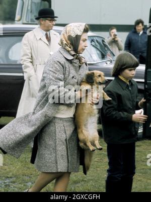 Königin Elizabeth II, begleitet von Lady Sarah Armstrong-Jones, trägt am 01. Mai 1977 einen ihrer Hunde im Windsor Great Park. Stockfoto