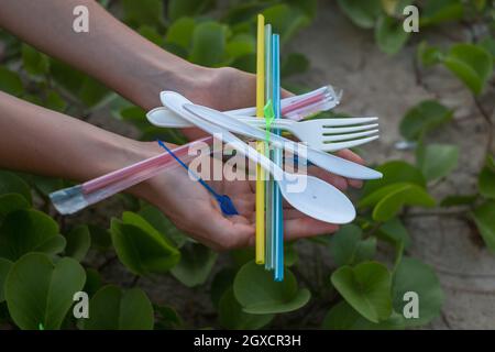 Hände, die gebrauchte Plastikschalen und Trinkhalme am Strand halten. Schönes grünes Gras auf dem Hintergrund. Umweltproblem. Einweg-Kunststoffabfälle Stockfoto