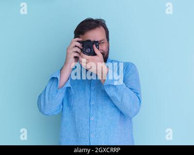 Porträt des männlichen Fotografen in blauem Hemd mit alten analogen slr-Art-Kamera, während sie vor cyanfarbenem Hintergrund stehen Stockfoto