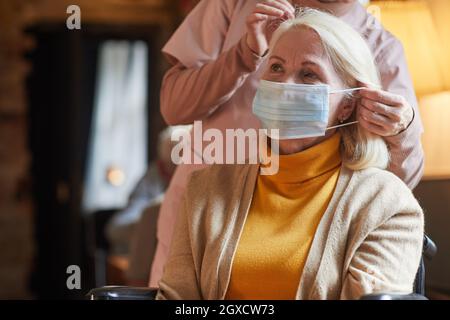 Porträt einer älteren Frau, die im Seniorenheim eine Maske trägt, mit einer Krankenschwester, die ihr hilft, Platz kopieren Stockfoto