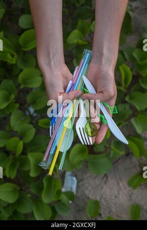 Hände, die gebrauchte Plastikschalen und Trinkhalme am Strand halten. Schönes grünes Gras auf dem Hintergrund. Umweltproblem. Einweg-Kunststoffabfälle Stockfoto