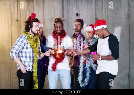 Multiethnische Gruppe junger happy and Business Leute Beleuchtung eine Wunderkerze und Spaß beim Silvester feiern in der betonwand an Stockfoto