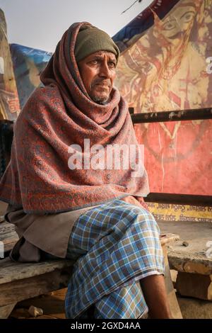 INDIEN, VARANASI - 27. NOVEMBER 2015: Ethnisch nachdenkliche männliche SitzungBlick weg auf Holzbank in schäbigen Dorf in Indien Stockfoto