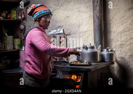 NEPAL, HIMALAYA - 6. NOVEMBER 2015: Seitenansicht von konzentrierten ethnischen Frauen in legerer Kleidung, die in der Nähe des Herdes stehen und heiße Speisen im Topf rühren Stockfoto