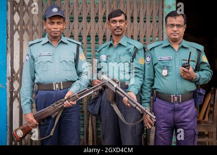 INDIEN, BANGLADESCH - 6. DEZEMBER 2015: Ethnisch bewaffnete Männer in Polizeiuniform und Mütze, die in der Nähe von Metalltoren eines verwitterten Gebäudes stehen und schauen Stockfoto