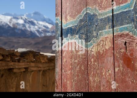 Alte Holzwand mit Kratzern und rissiger Gebäudefarbe, umgeben von hohen schneebedeckten Berggipfeln in Nepal Stockfoto