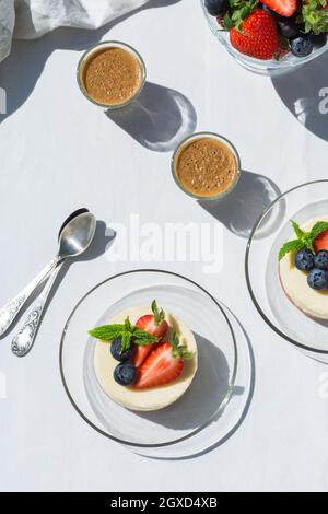 Leckere Käsekuchen mit frischen Erdbeeren und Heidelbeeren unter Minzblättern gegen Espresso-Kaffee auf dem Tisch in der Cafeteria Stockfoto