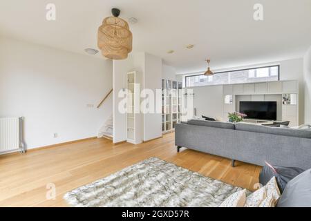 Moderne Wohnzimmereinrichtung mit Kissen auf der Couch gegen blühende Blumen in Vase auf dem Tisch unter Lampe im Haus Stockfoto