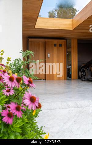 Luxus Villa Hof mit blühenden Blumen und moderne Auto in der Garage mit Holzwänden und Aufzug geparkt Stockfoto