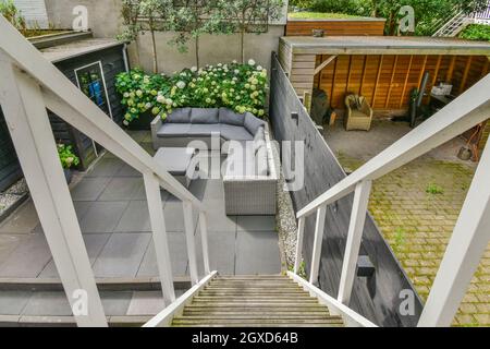 Von oben auf dem Hinterhof mit Treppe gegen Sofa zwischen Tisch und blühenden Blumen am Tag Stockfoto