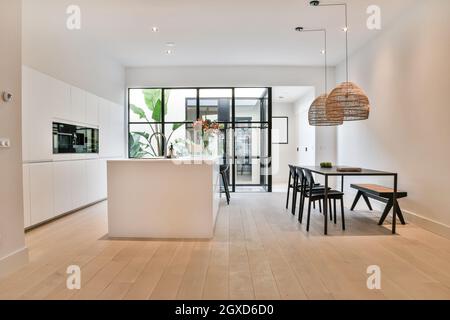 Tisch unter Lampen gegen eingebaute Elektrogeräte in moderner Küche im Haus mit Parkett Stockfoto