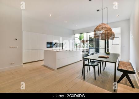 Tisch unter Lampen gegen eingebaute Elektrogeräte in moderner Küche im Haus mit Parkett Stockfoto
