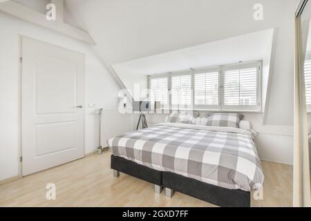 Komfortables, weiches Bett mit weißer Federdecke in der Nähe großer Fenster im modernen Schlafzimmer des Apartments Stockfoto