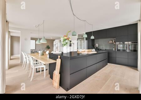 Stilvolles Interieur mit geräumiger Küchenecke mit schwarzen Möbeln und Holztisch in moderner Wohnung tagsüber Stockfoto