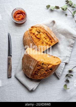 Blick von oben auf frisch gebackenen Laib Brot und rote Pesto-Sauce in Glas serviert auf dem Tisch mit Serviette und Messer Stockfoto