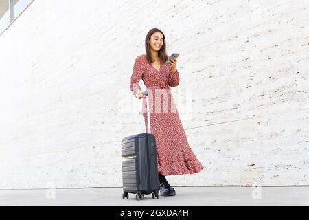 Fröhlicher junger asiatischer Mann mit dunklen Haaren in lässigem Outfit Und die Kopfhörer lächeln, während sie Videoanruf auf dem Laptop führen City Street Stockfoto