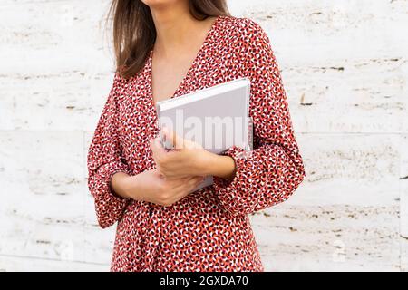 Cropped unkenntlich weiblich in stilvoller Kleidung stehend mit Buch gegen weiße Wand am Tag Stockfoto