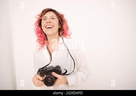 Lächle Fotografin mit rosa Haaren und halte eine professionelle Fotokamera in den Händen im hellen Raum Stockfoto