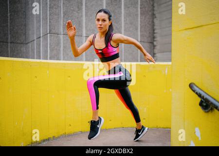 Eine athletische Frau in einem rosa Sportoutfit, die in einer urbanen Umgebung läuft Stockfoto