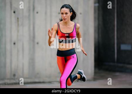 Eine athletische Frau in einem rosa Sportoutfit, die in einer urbanen Umgebung läuft Stockfoto