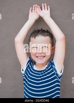 Lächelnder Junge mit nassem Haar in gestreiftem T-Shirt und Blick auf die Kamera an der Holzwand Stockfoto