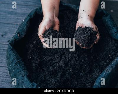 Hohes Erntewinkel unkennbares Kind, das die Hände ausstreckend und tagsüber trockene Erde gegen den Blumentopf demonstrierte Stockfoto