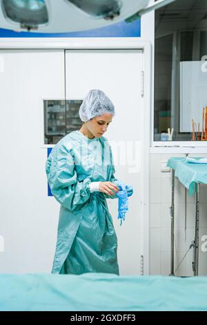 Junge Tierärztin in grüner Uniform, die in der Klinik sterile Handschuhe aufsetzt Stockfoto