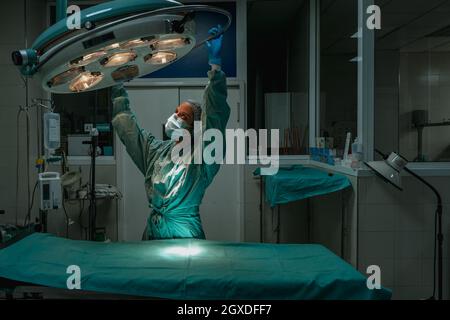 Junge weibliche Tierärztin in einer chirurgischen Uniform und sterilen Maske, die nach oben schaut, während sie die Lampe über dem medizinischen Textil in der Klinik justiert Stockfoto