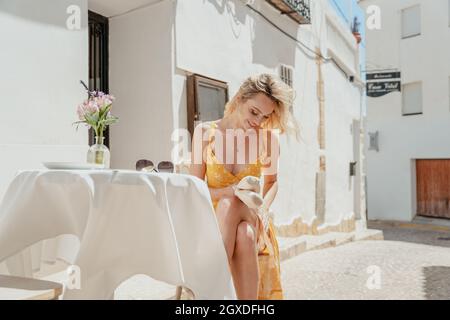 Friedliche weibliche Ballerina, während sie mit gekreuzten Beinen am Tisch sitzt und die spitzenschuhe anschaut, die er in der Altstadt in der Hand hält Stockfoto