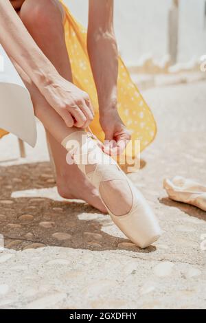 Crop unerkennbare Ballerina trägt langes Kleid und spitzenschuh sitzen auf einem Stuhl auf der Straße Stockfoto