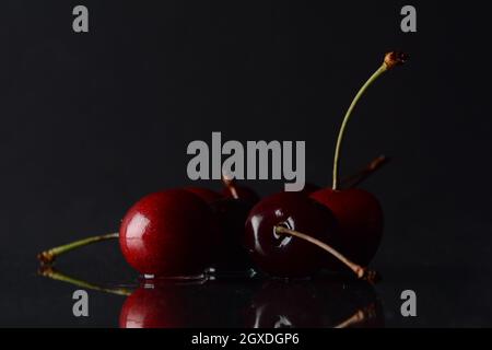 Kirschen, mit Wassertropfen auf schwarzem Hintergrund mit Spiegelung Stockfoto